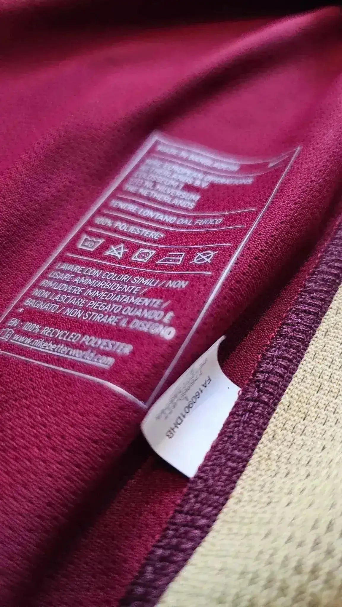 Care label showing fabric composition and washing instructions on red football shirt.