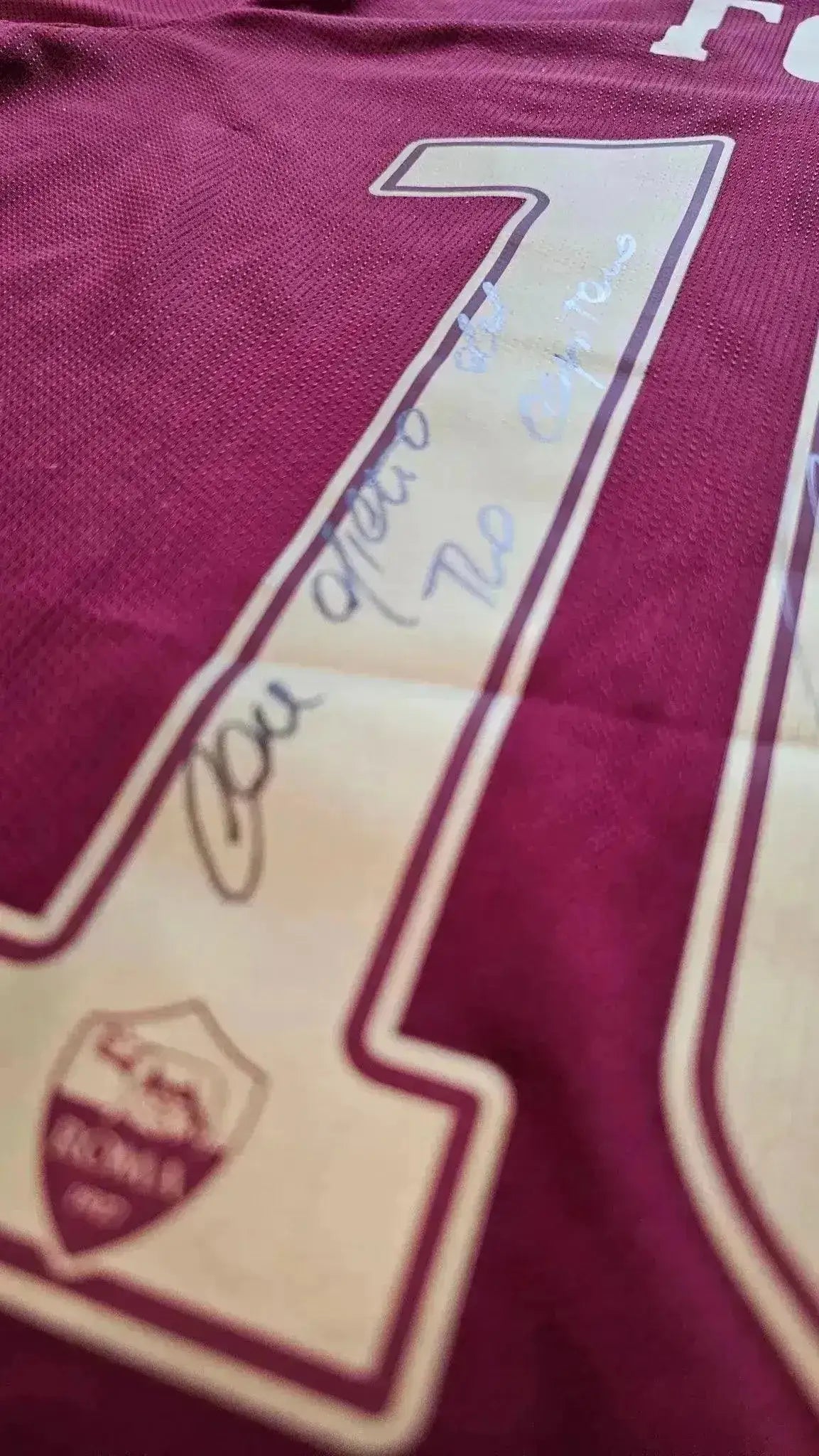 Detail showing signature near No. 10 on red and gold A.S. Roma football shirt.