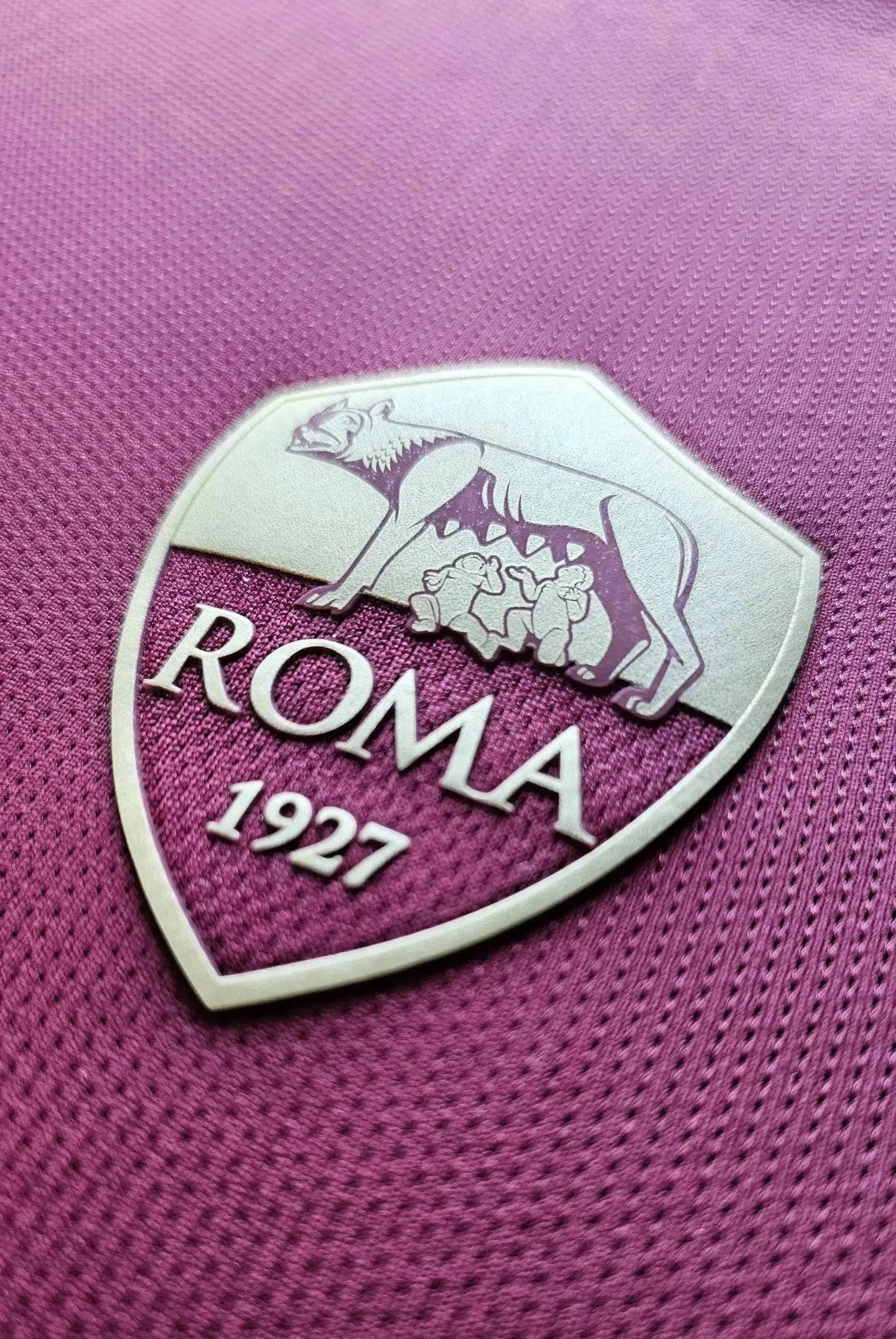 Detail of A.S. Roma crest featuring a wolf with roman she-wolves and text 'ROMA 1927'.