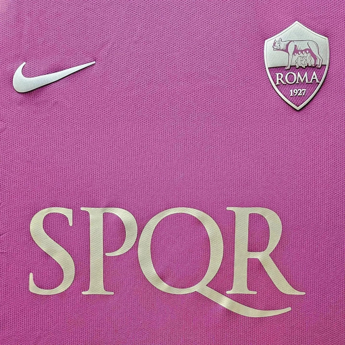 Detail view featuring the gold 'SPQR' text and A.S. Roma crest on a pink football shirt.
