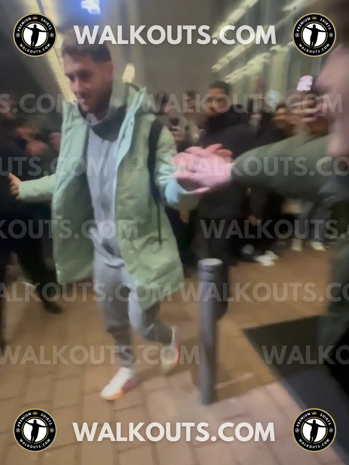 Santiago Gimenez in a green jacket being escorted by security through a crowd, with &