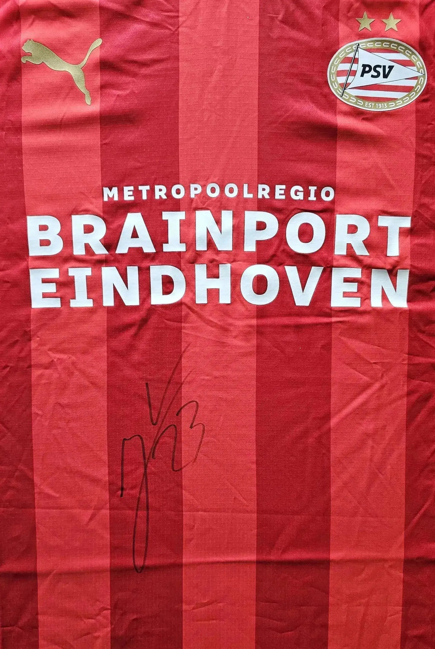 Crest of PSV Eindhoven with two stars and signature of player Veerman on red soccer jersey.