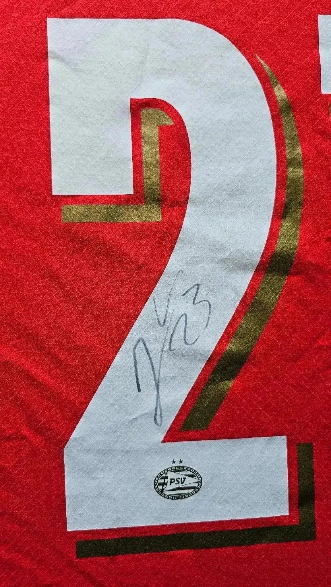 Detail showing No. 23 and signature on red PSV soccer jersey with club crest.