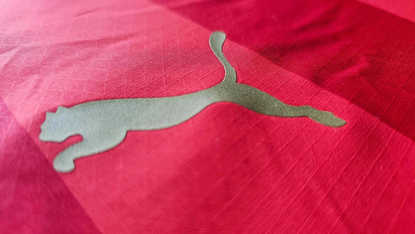 Close-up of the Puma logo in metallic silver on a red soccer jersey background.