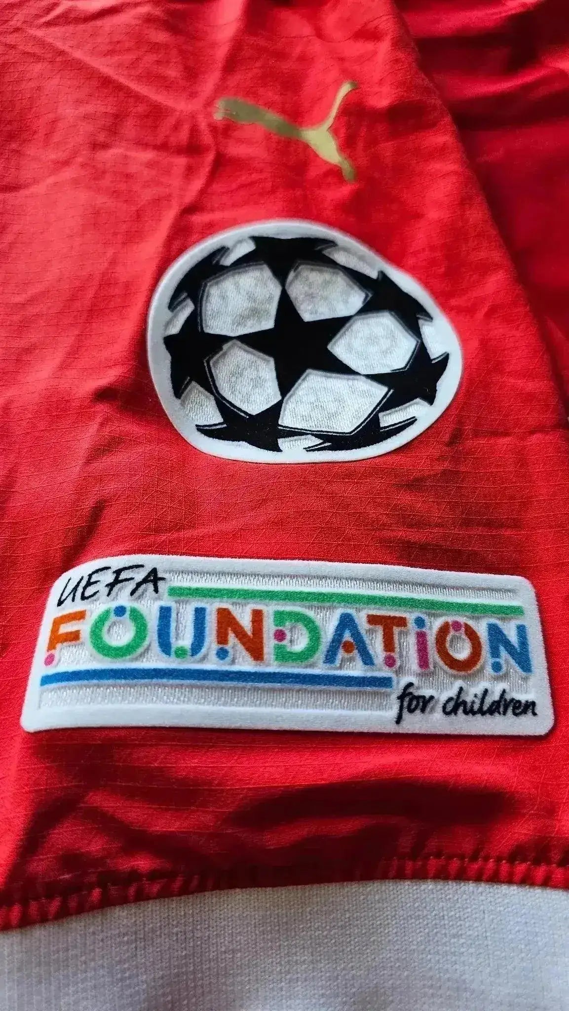 Red shirt featuring UEFA Foundation for Children patch and black Champions League crest.