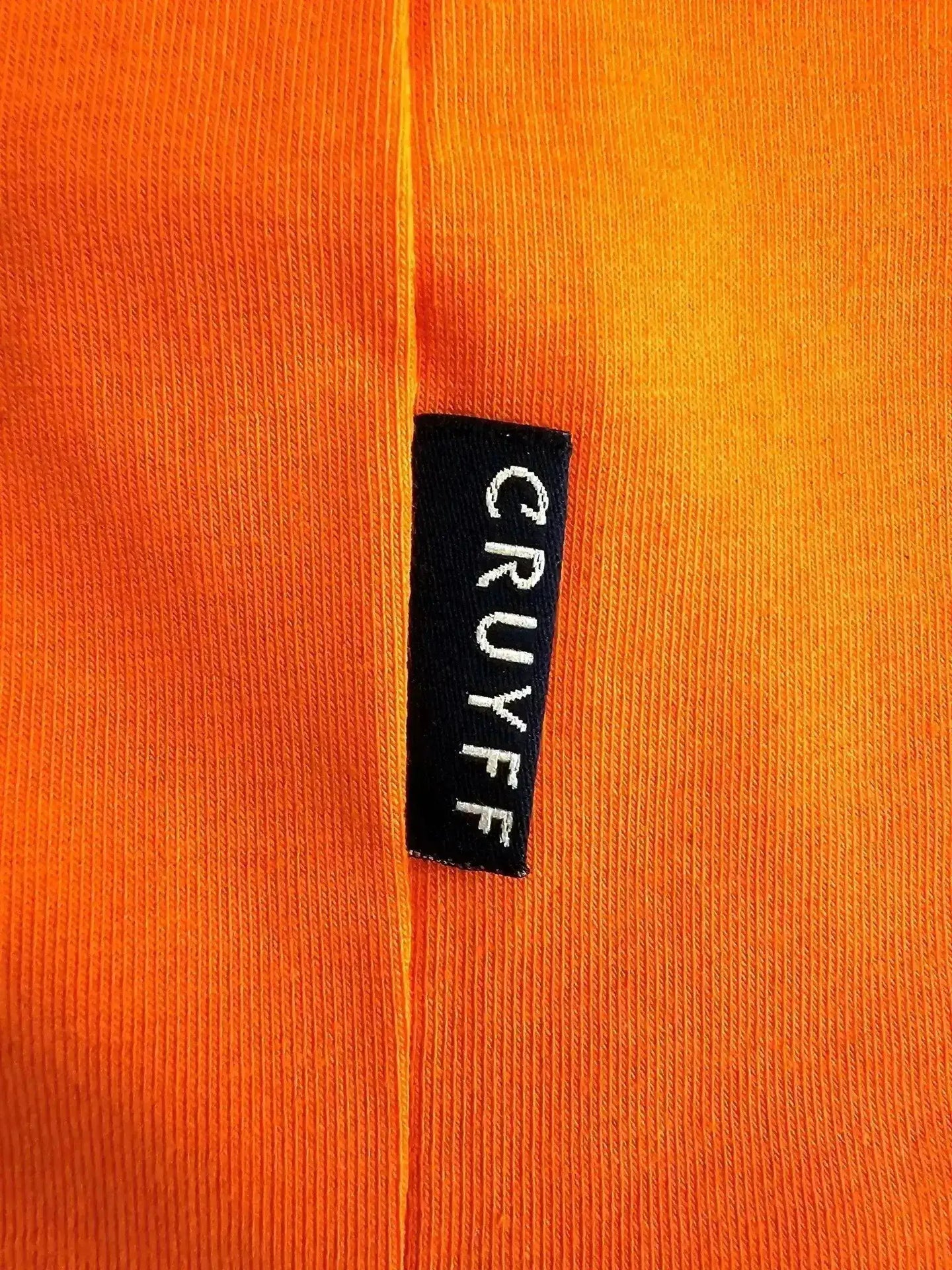 Close-up of the label showing 'CRUYFF' on an orange football shirt.