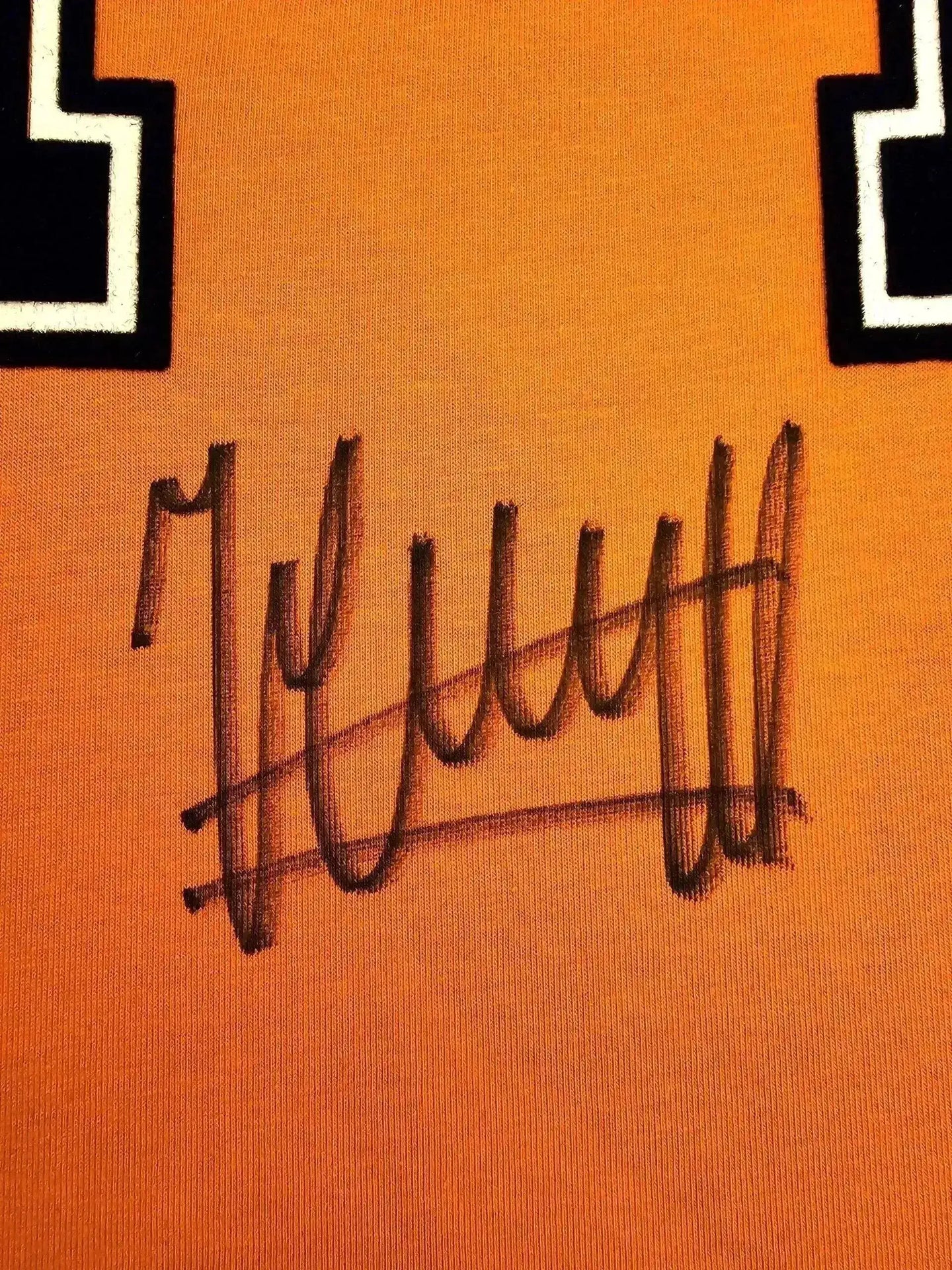 Close-up of Johan Cruyff's signature on orange football shirt with black and white details.