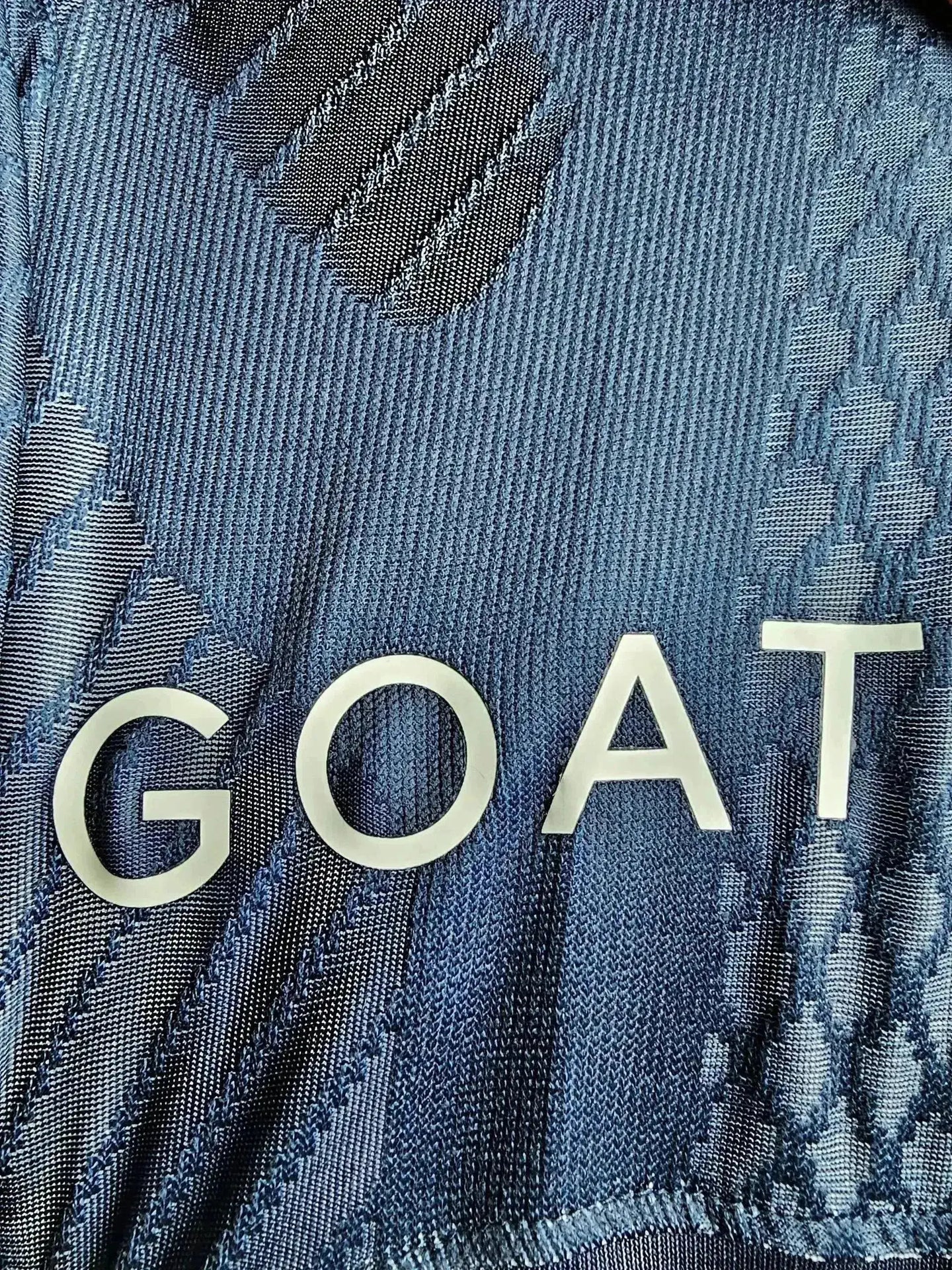 Close-up showing the word 'GOAT' in silver on the blue fabric with textured patterns.