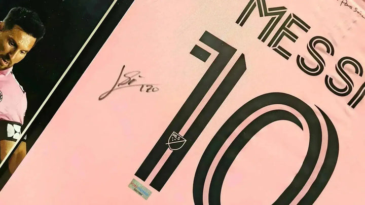 Detail view showing the signature of Messi and squad number 10 on a pink soccer jersey.