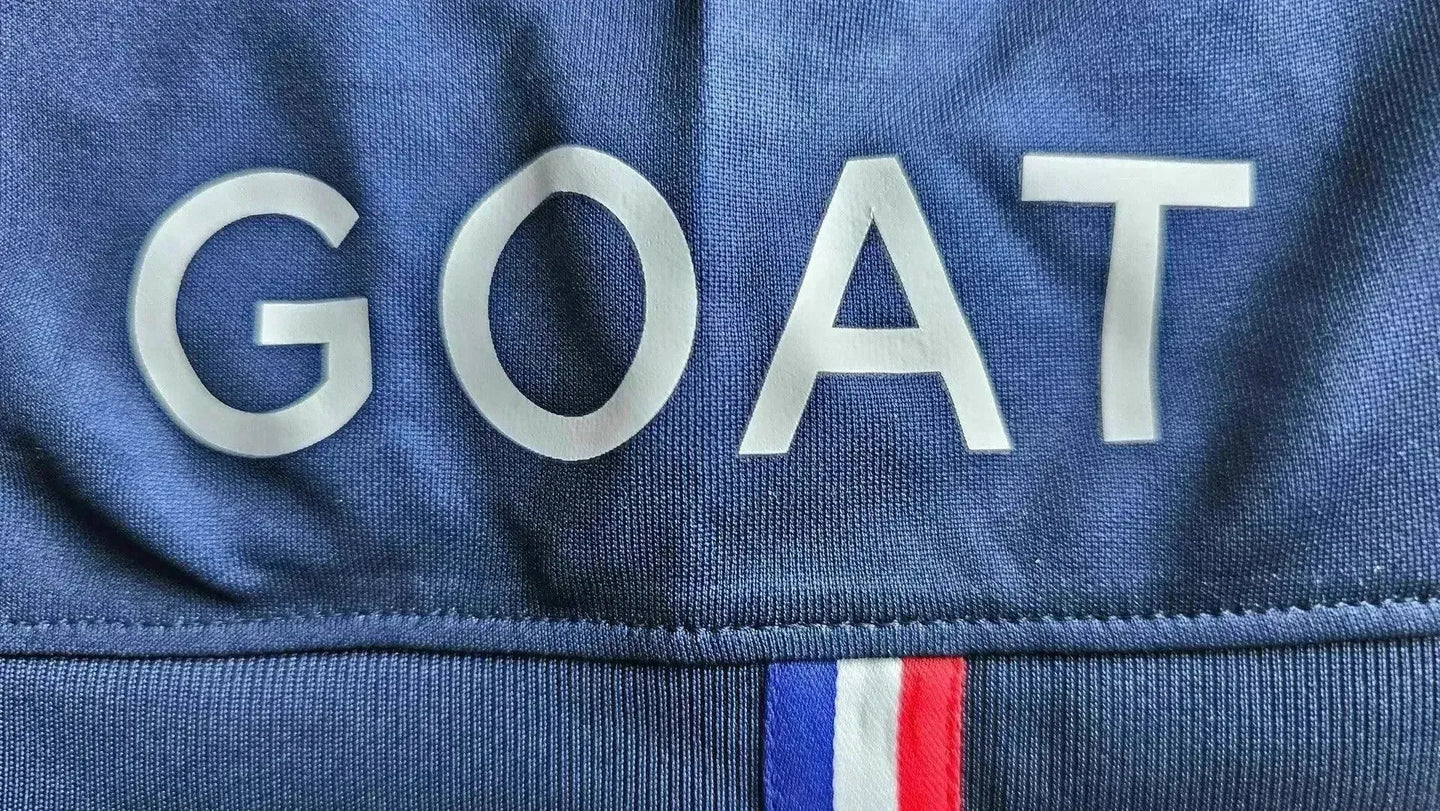 Close-up of the word 'GOAT' on the signed soccer jersey with a tricolor detail underneath.