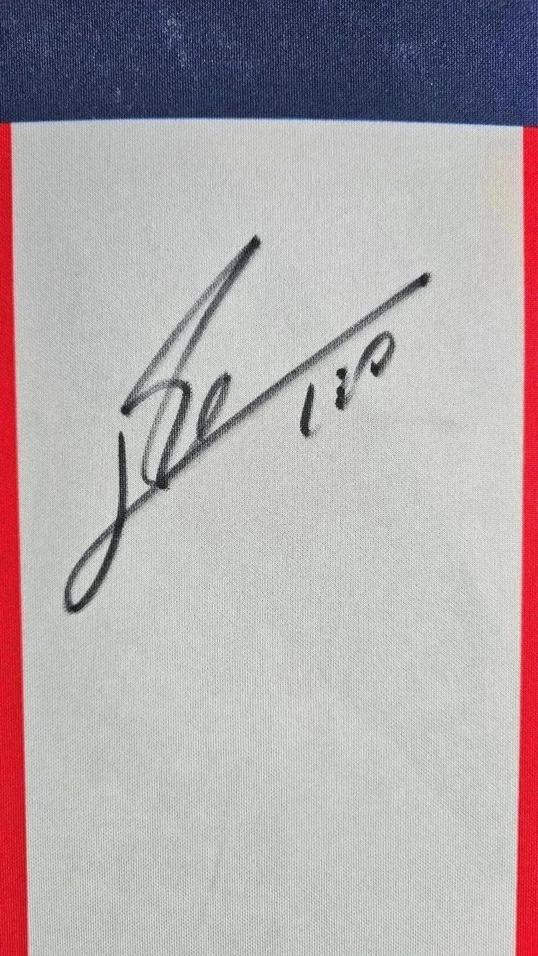 Signature detail of Lionel Messi on a PSG soccer jersey with red accents.