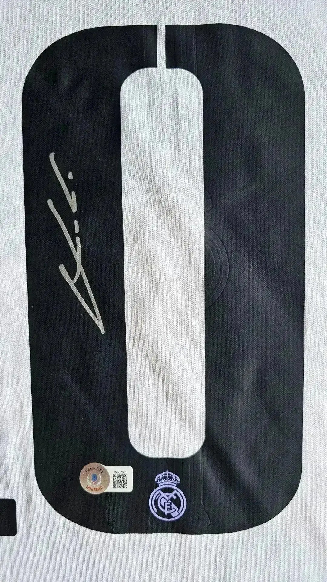 Detail showing signature and No. 10 on black and white Real Madrid soccer jersey.