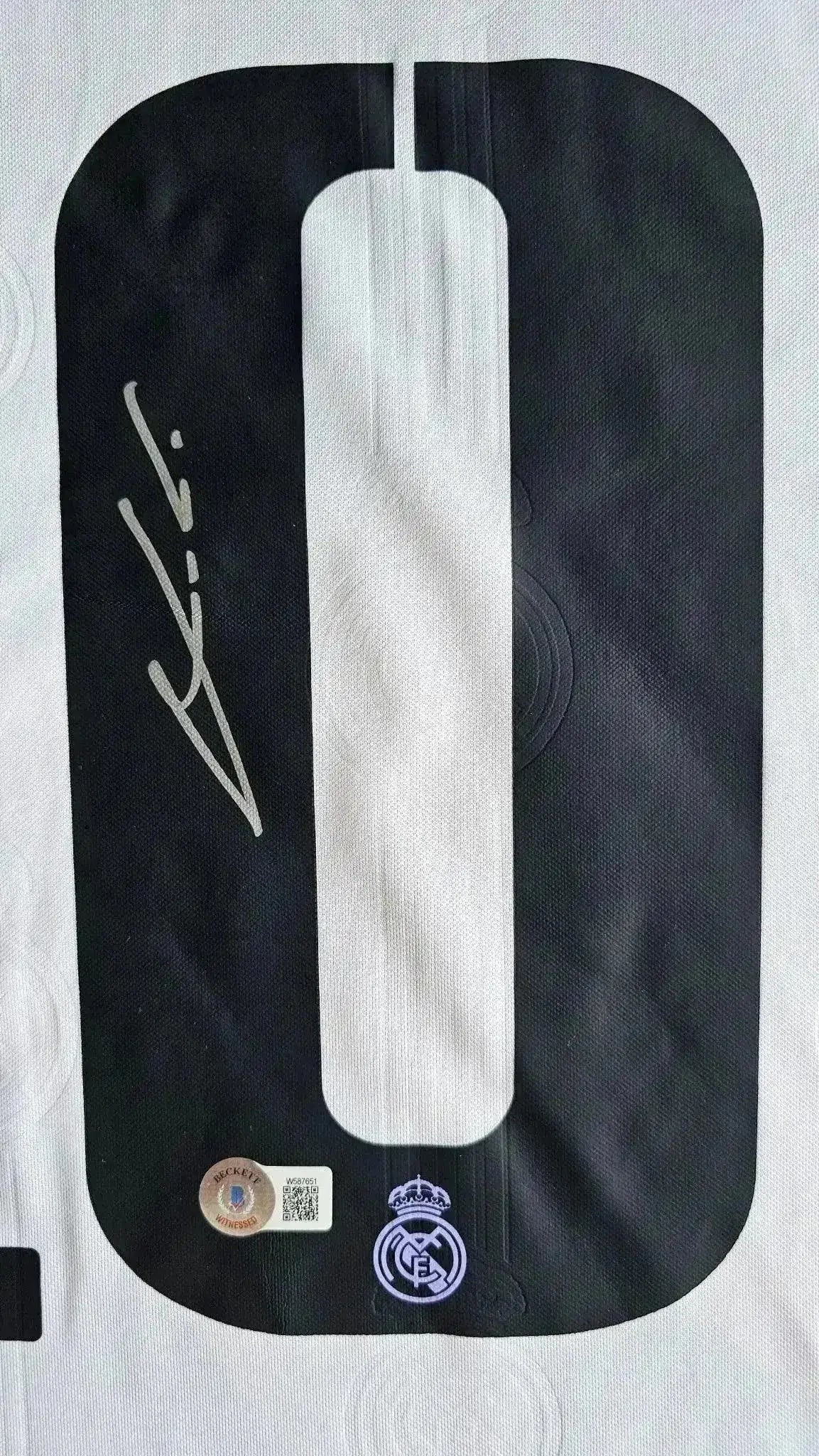 Detail showing signature and No. 10 on black and white Real Madrid soccer jersey.