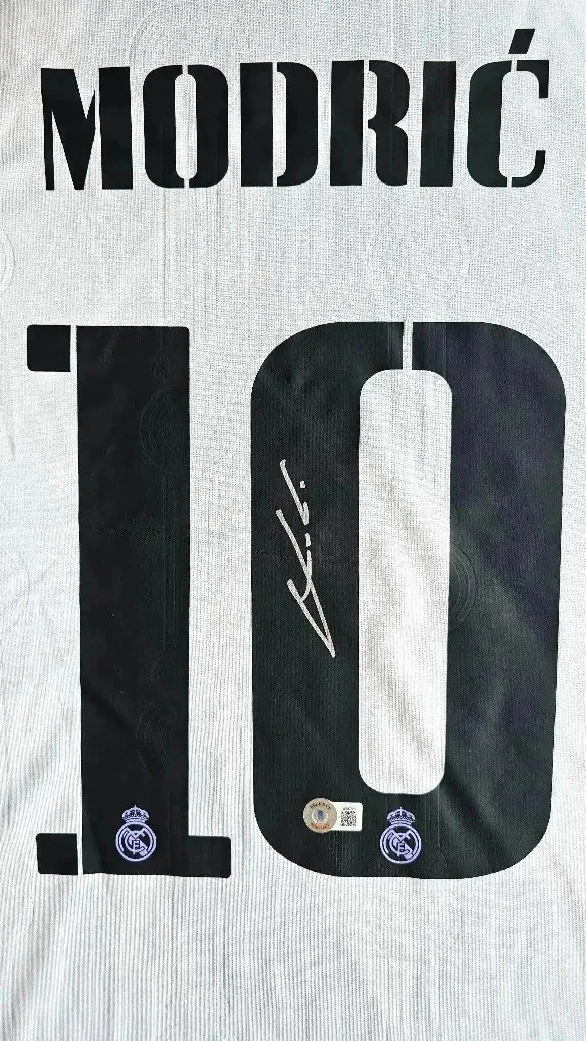 Detail view showing signature and No. 10 in black on a white Real Madrid soccer jersey.