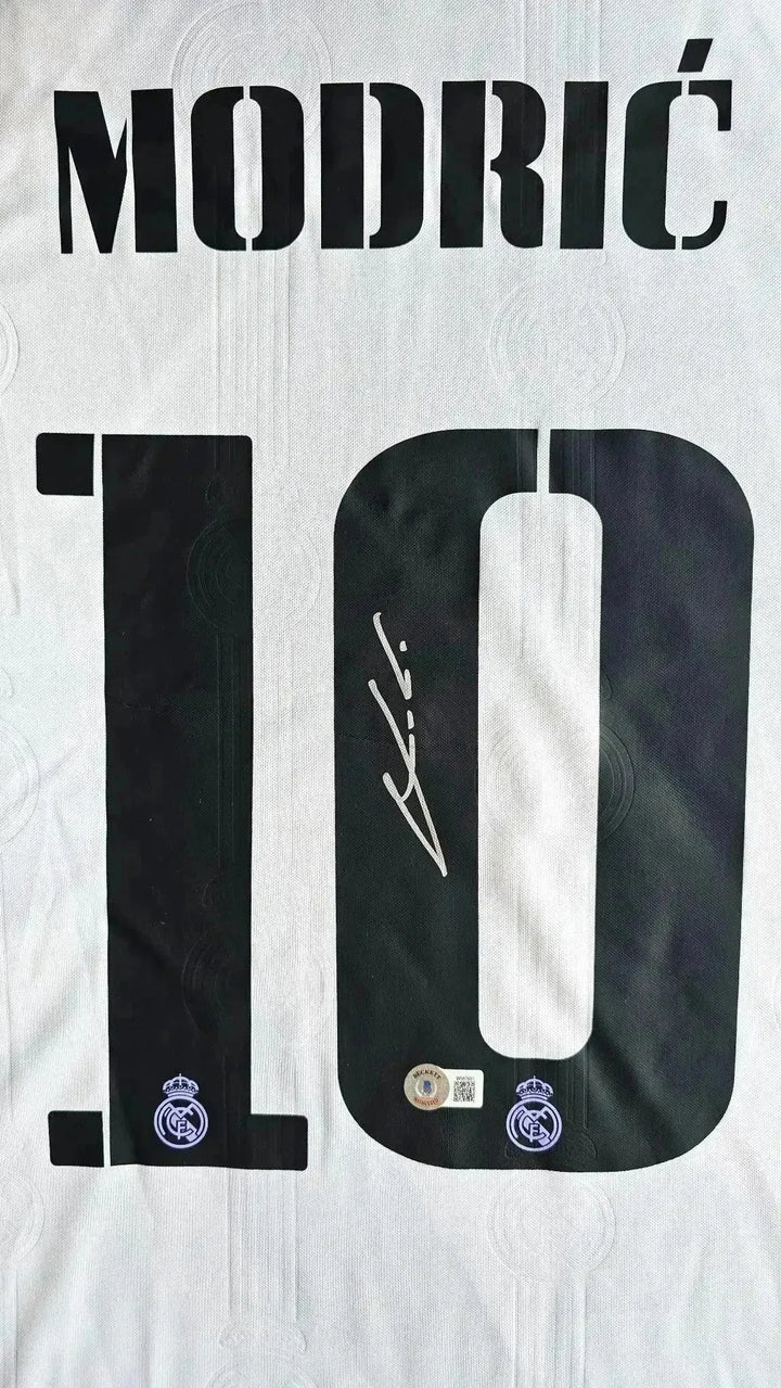 Detail view showing signature and No. 10 in black on a white Real Madrid football shirt.