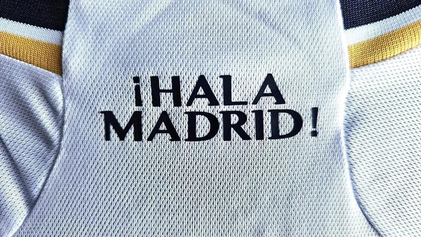 Crest detail showing the text ¡HALA MADRID! on the white fabric of the football shirt.