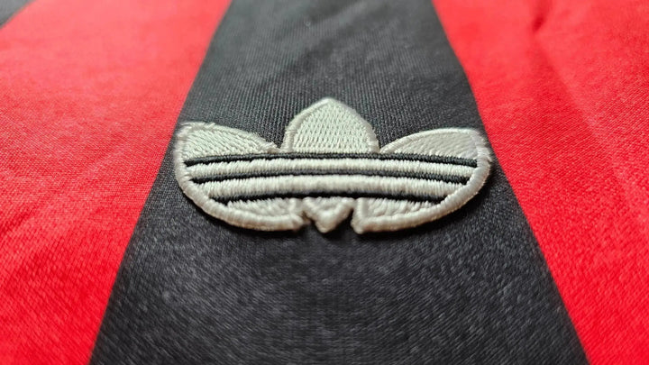 Close-up of the embroidered adidas logo on a red and black striped football shirt.