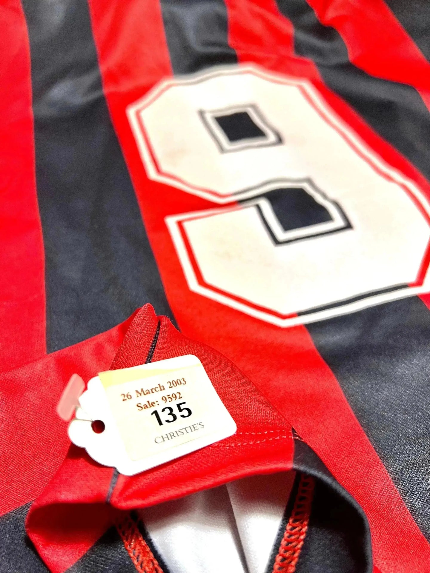 Close-up of No. 9 on red and black striped football shirt with Christie's tag showing sale details.
