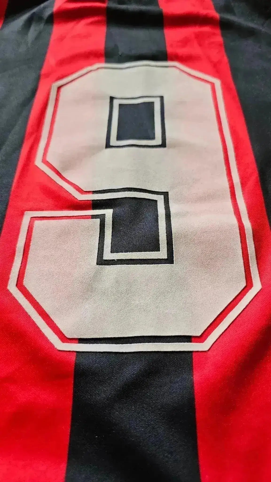 Detail view of No. 9 in white outlined in black on a red and black striped football shirt.
