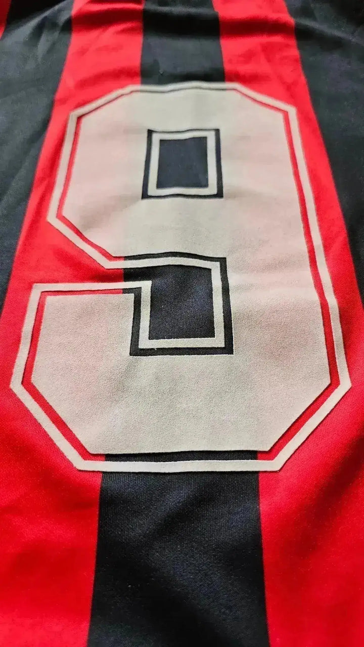 Detail view of No. 9 in white outlined in black on a red and black striped football shirt.