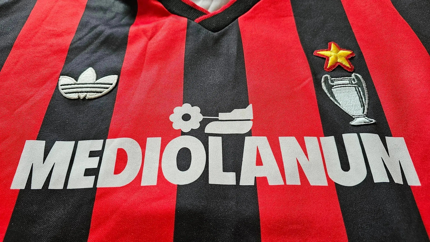 Detail view showing the AC Milan crest, MEDIOLANUM sponsor, and Adidas logo on a striped red and black shirt.