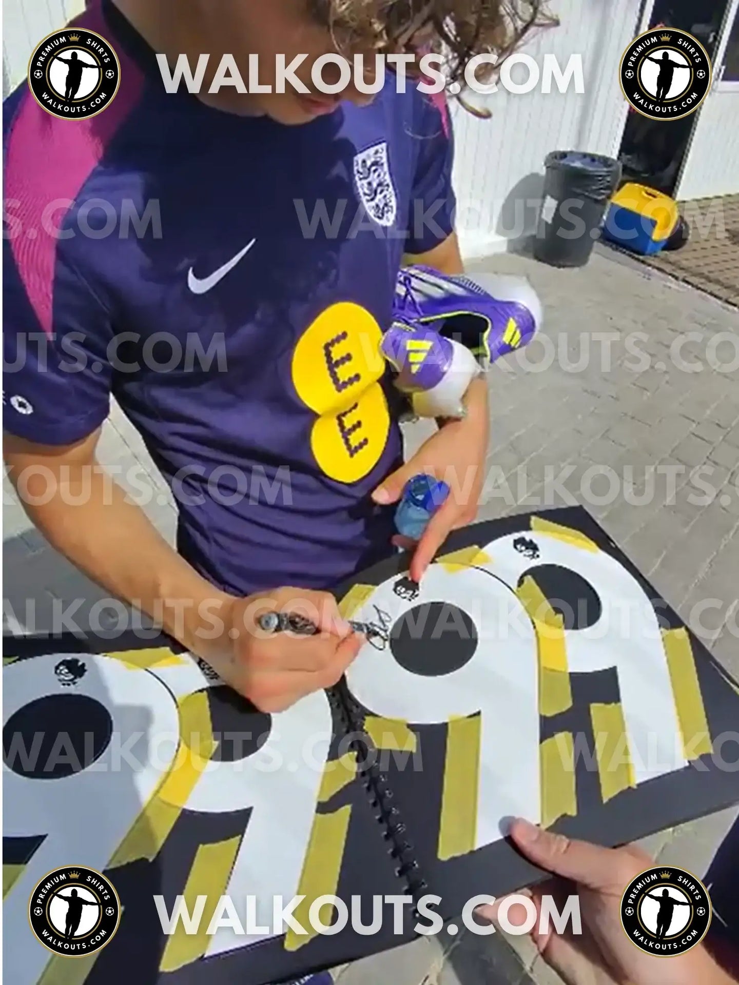 Max Dowman signing a black folder with yellow and black jersey numbers 99 visible.