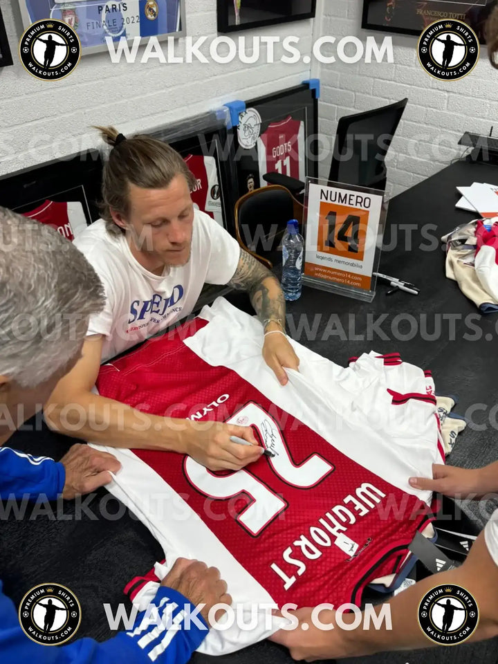 Wout Weghorst signs his No. 25 Ajax football shirt, featuring red and white colors with a visible signature.