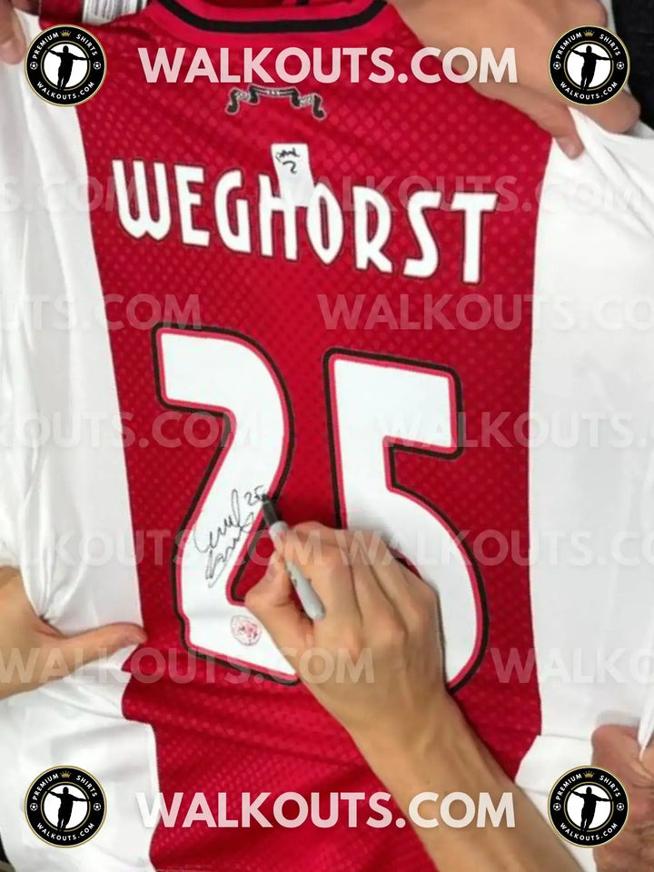 Wout Weghorst signing the No. 25 AFC Ajax football shirt with a black pen.