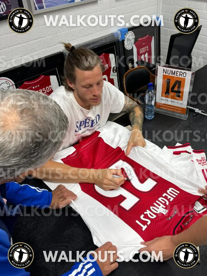Wout Weghorst signing a red and white Ajax football shirt with No. 25 visible.