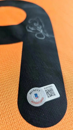 Signature detail on the No. 9 with Beckett authentication sticker visible. Orange background.