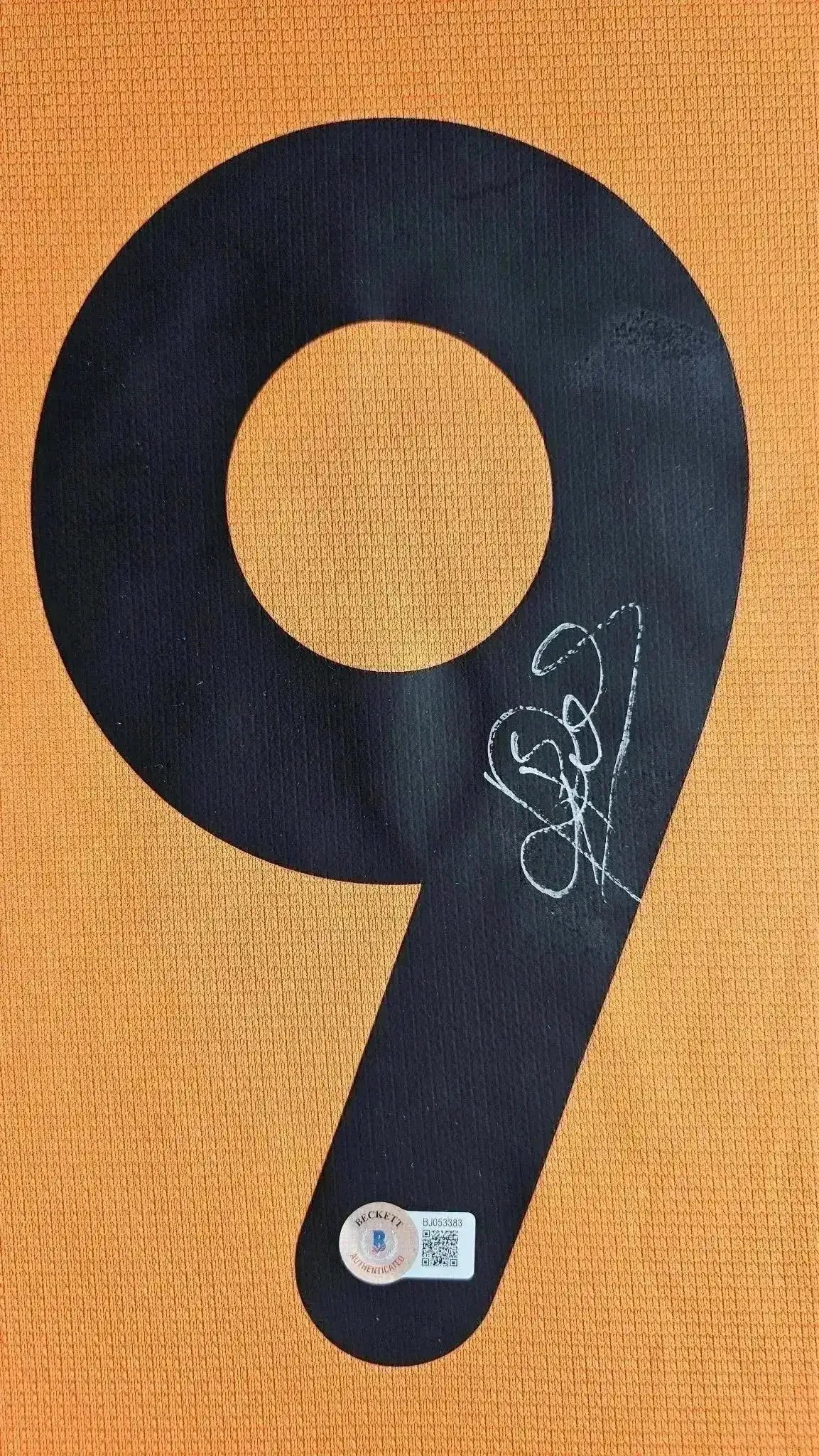 Close-up of No. 9 in black with signature on orange background and Beckett authentication sticker.