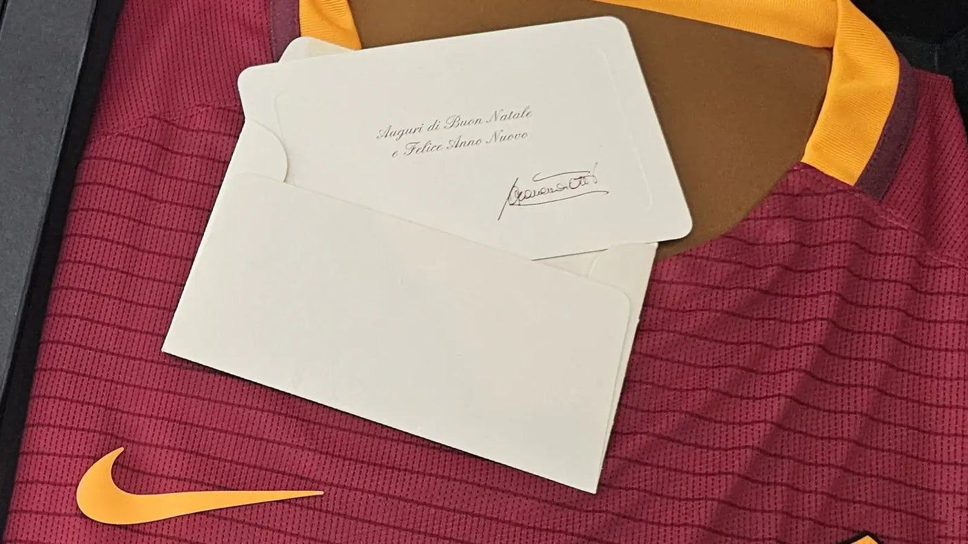 Maroon AS Roma football shirt with orange accents and a white card on top.