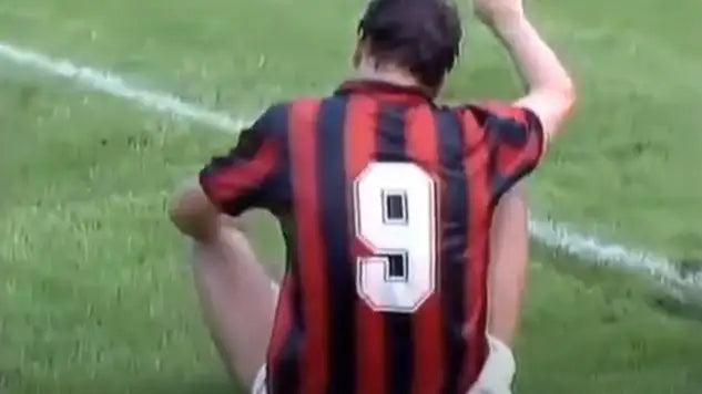 Marco van Basten wearing a red and black striped AC Milan football shirt with number 9 on a grassy field.