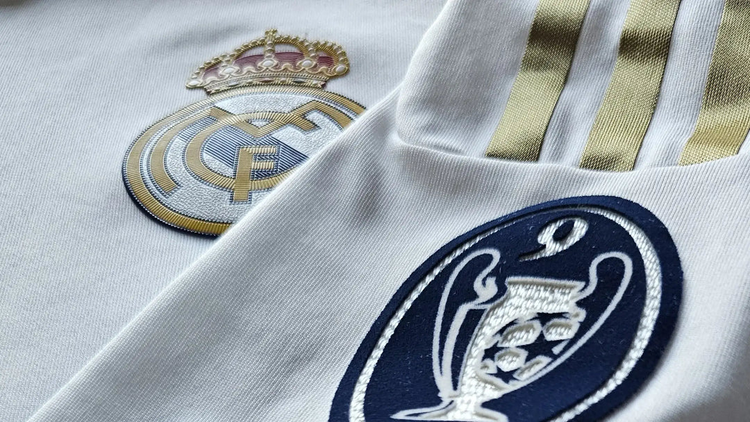 Close-up of a Real Madrid football shirt with a logo and text and Chamipions League batch on a white fabric background.