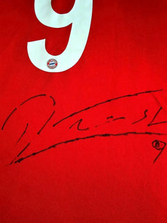 Detail of No. 9 and signature on a red soccer jersey featuring FC Bayern München crest.