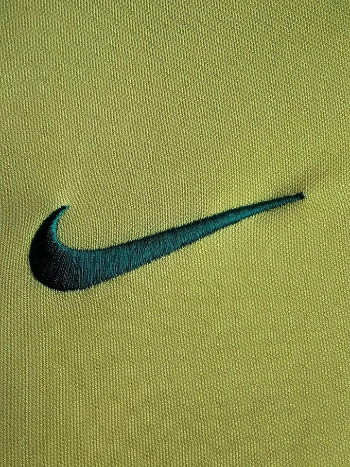 Detail view of the embroidered Nike logo in teal on a yellow fabric background.