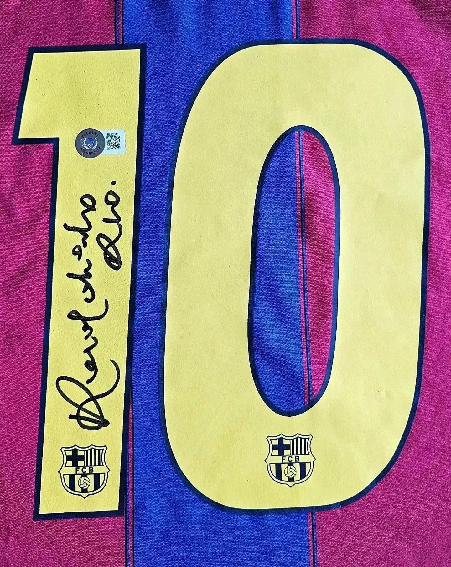Detail showing No. 10 and Ronaldinho's signature on Barcelona soccer jersey with club crest.