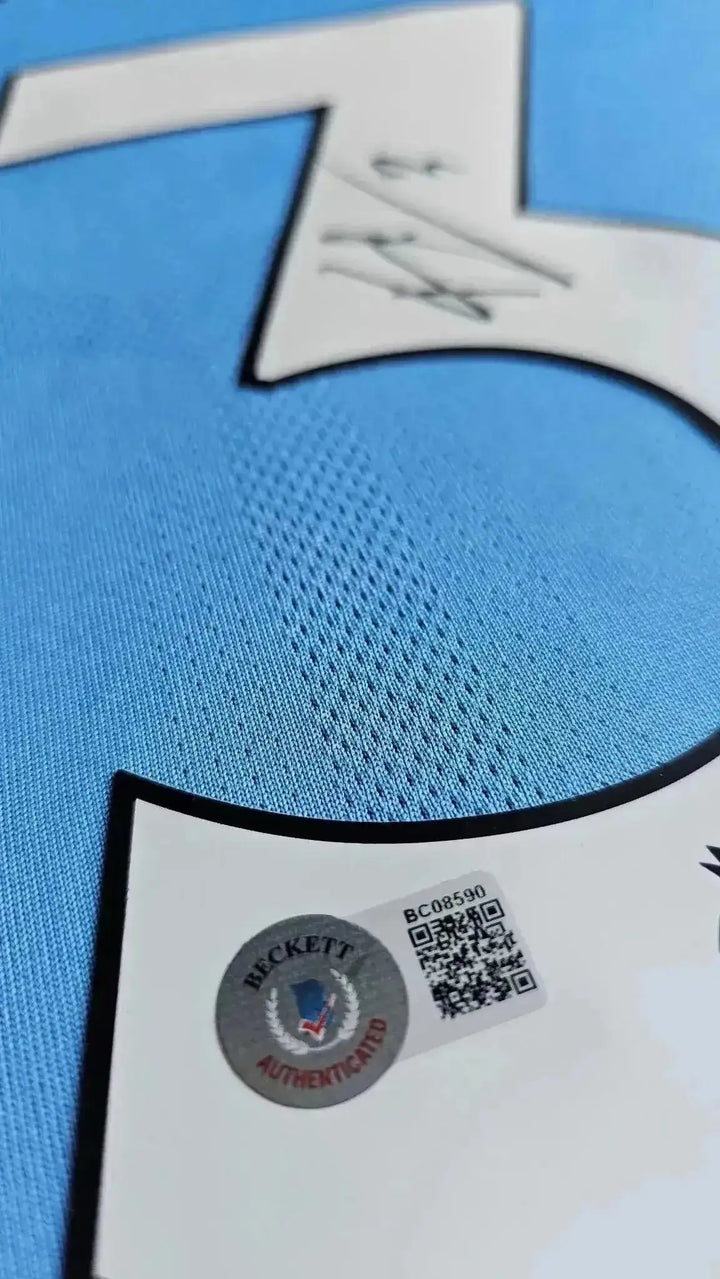 Close-up showing signature on No. 3 and Beckett authentication detail on blue football shirt.