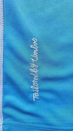 Close-up of the embroidered text 'Tailored by Umbro' on a blue soccer jersey.