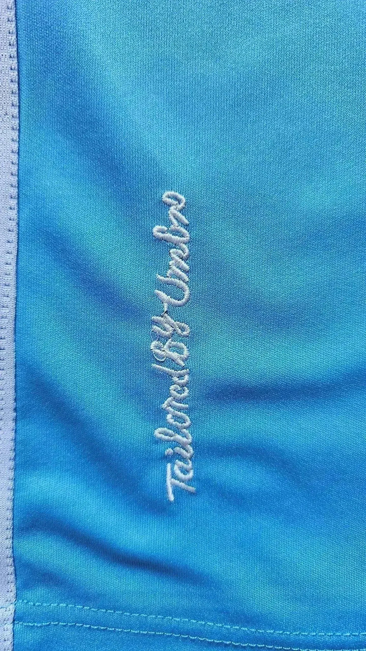 Close-up of the embroidered text 'Tailored by Umbro' on a blue football shirt.