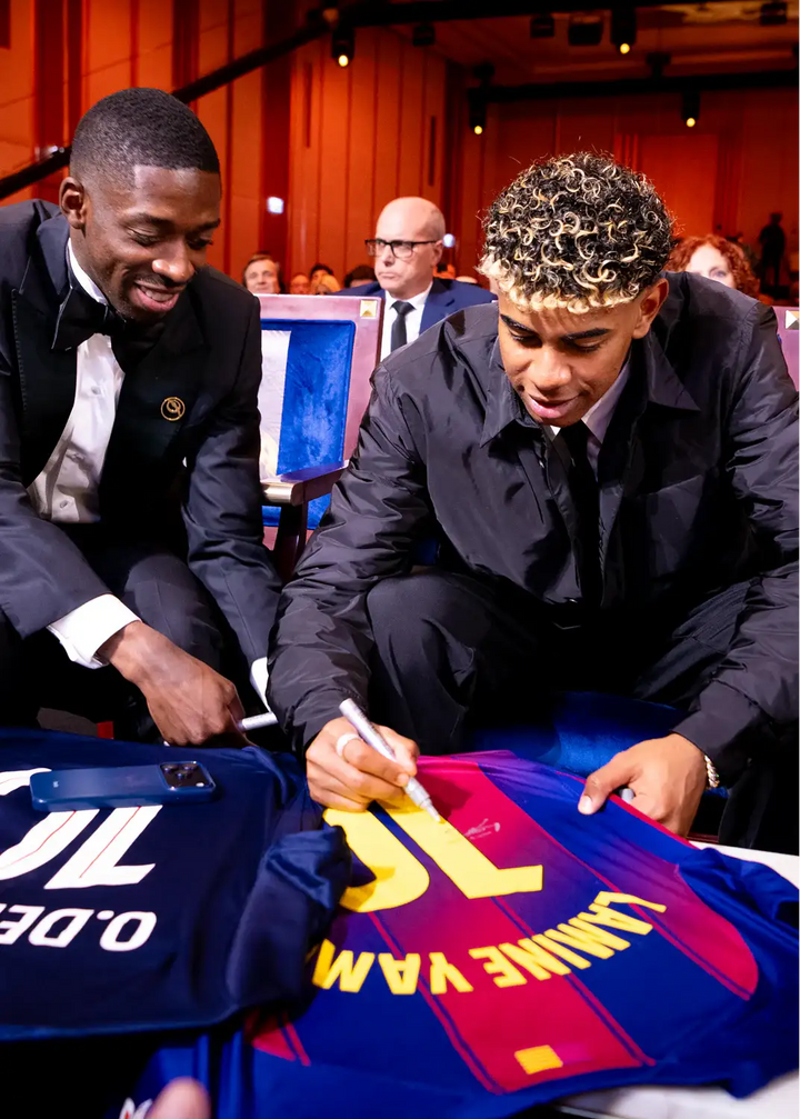 Lamine Yamal signing his No. 10 FC Barcelona soccer jersey with navy, yellow, and purple colors.