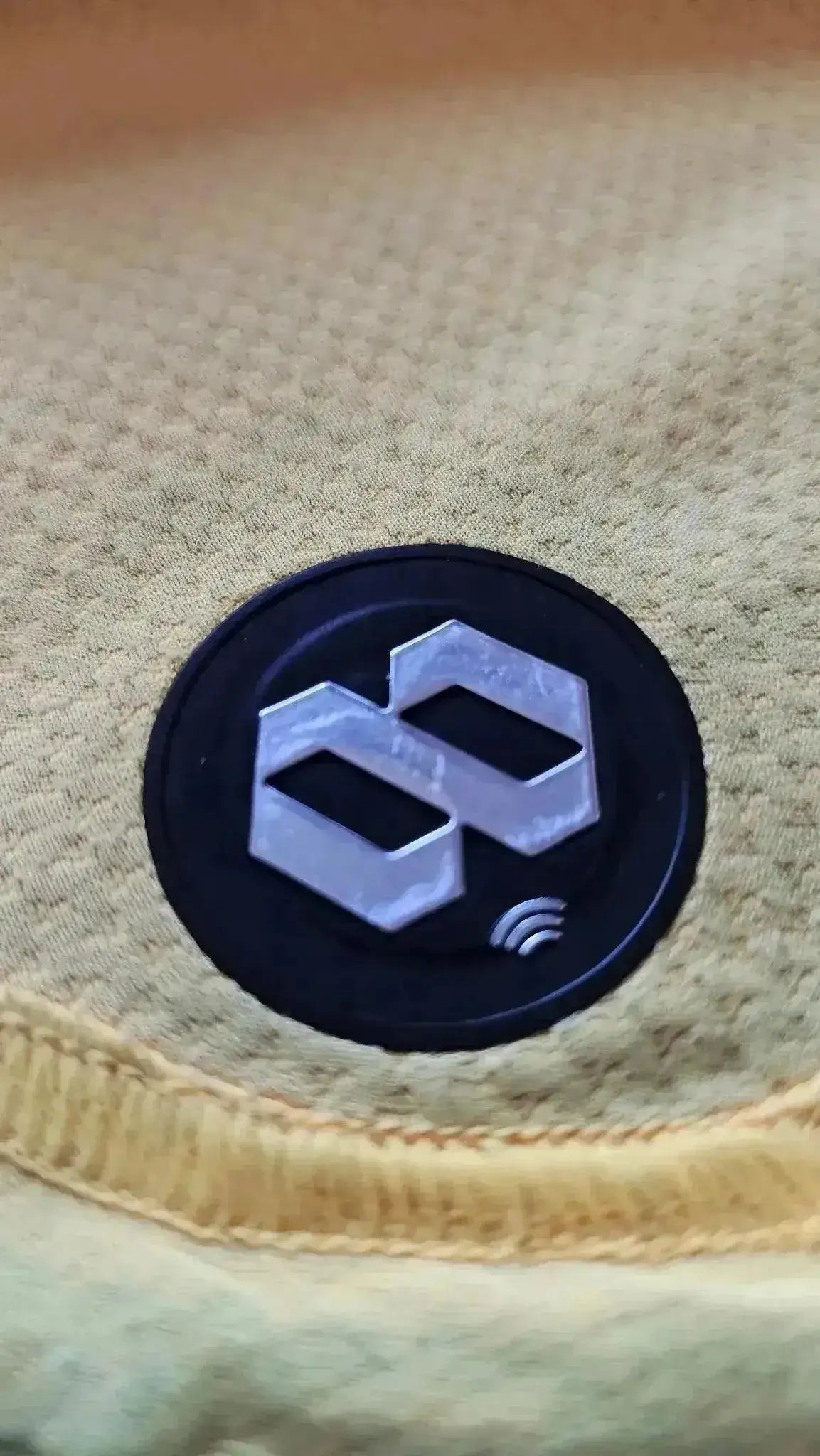 Detail view of the black circular patch with the logo on a yellow fabric background.