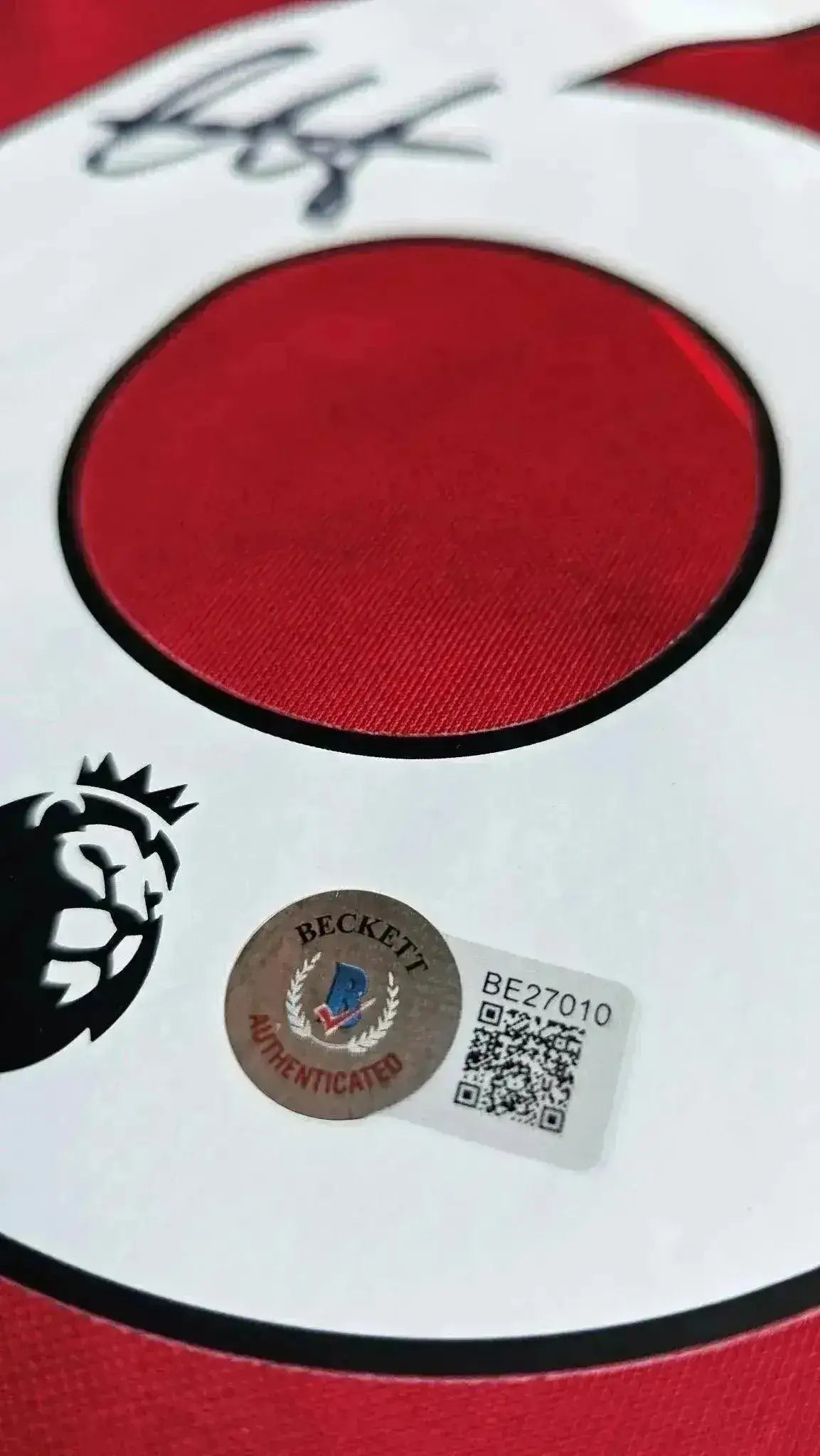 Close-up of signed detail and Beckett authentication sticker on red soccer jersey.