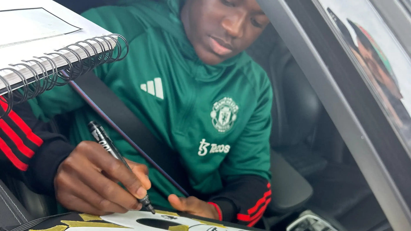Kobbie Manioo in a green sports jersey signing a nameset inside a vehicle.