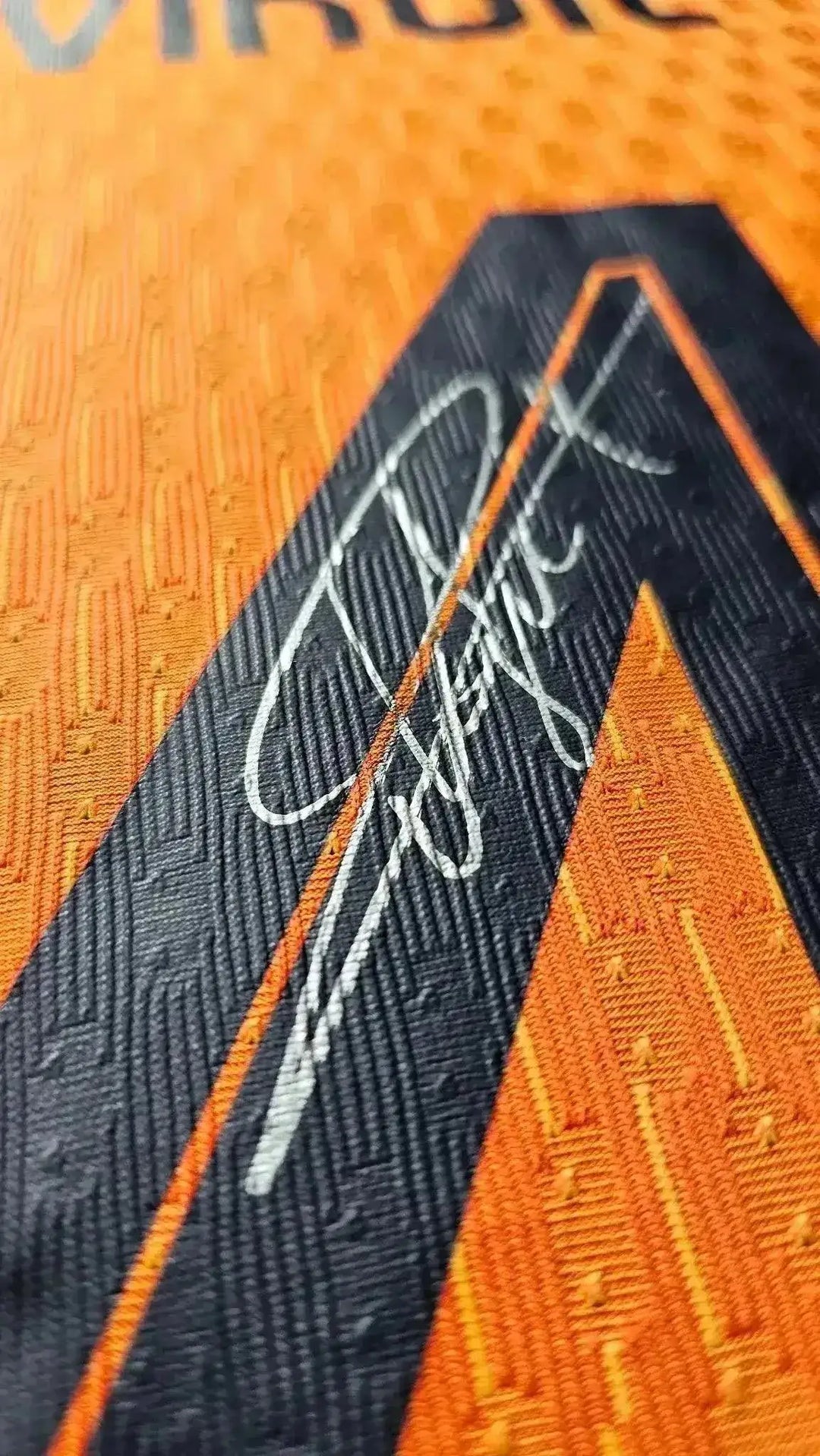 Close-up of signature on orange football shirt with black detailing.