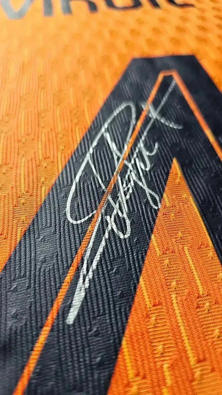 Close-up of signature on orange football shirt with black detailing.