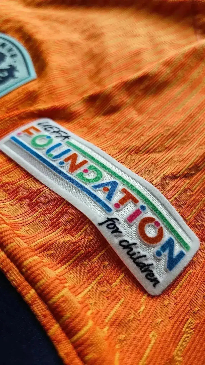Close-up of the UEFA Foundation for Children logo on an orange football shirt.