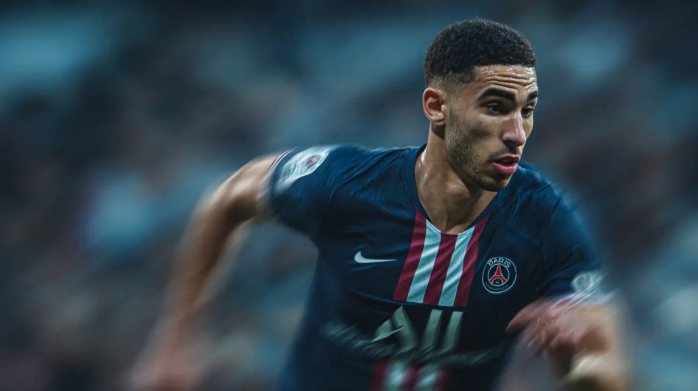 Achraf Hakimi sprinting for Paris Saint-Germain, navy kit with central stripes, motion blur during a night match.