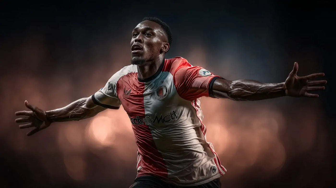 Antoni Milambo of Feyenoord celebrating with arms wide, red and white home shirt, side profile under soft stadium lights.