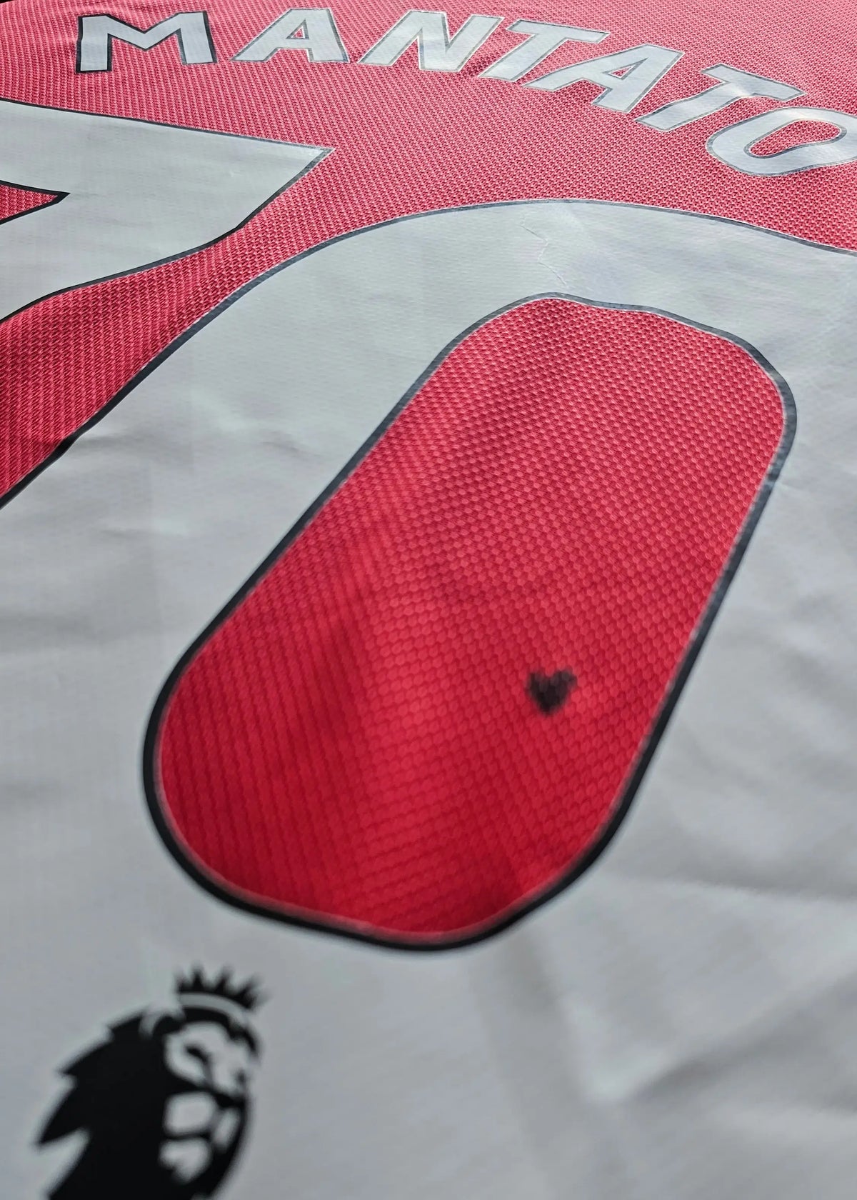 Close-up of the MANTATO lettering beside No. 70, a small heart-shaped mark and the Premier League crest on the white panel, Manchester United F.C. shirt.